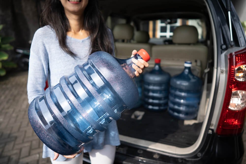 Woman loads large water jugs into trunk of car